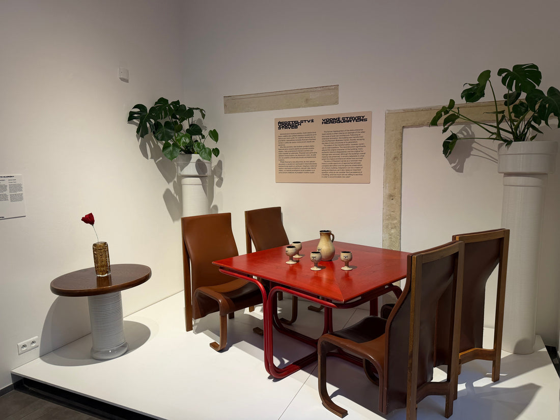 Expozice výstavy HNUSNÝ v Design Museum Prague: červený stůl, hnědé židle, keramika a bílé stojany s rostlinami.